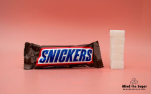 A photo of Snickers bar with 4 cubes of sugar.